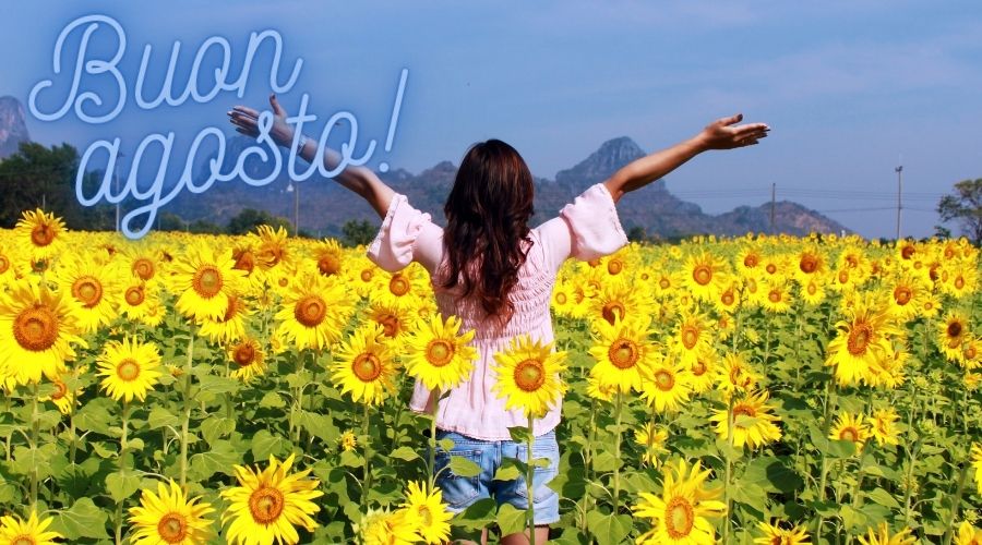 fotografia di donna con le braccia al cielo, in un campo di girasoli con le montagne sullo sfondo